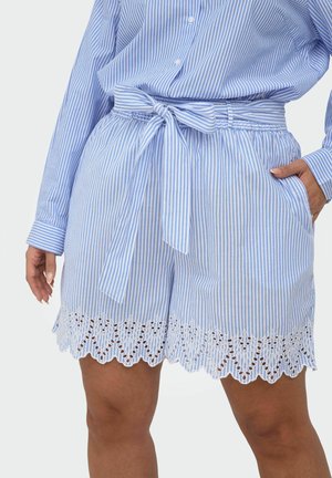 Kvinde iført blå og hvide lodrette stribede shorts med bundet bælte og flagrende blondekant, kombineret med en matchende stribet skjorte.