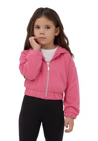 Felpa corta rosa realizzata in tessuto morbido, con zip, tasca frontale e polsini a costine, abbinata a leggings neri.