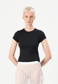 Tricou negru ajustat, dintr-un material neted, cu mâneci scurte și decolteu rotund. Purtați-l cu un strat inferior din dantelă albă.
