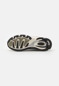 La semelle de la sneaker présente un motif en vagues en noir et beige, avec une surface de grip texturée et des accents contrastants en gris et olive.