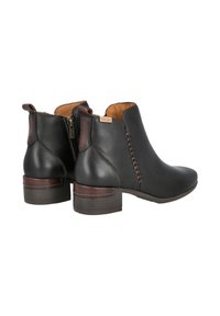Botas de tobillo de cuero negro con acentos marrones, que cuentan con una cremallera lateral, detalles de costura y tacones de madera gruesa. Textura suave.