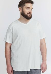 Hvid bomulds T-shirt med V-hals, korte ærmer, løs pasform og glat tekstur. Fremhævet med en subtil kant og et enkelt, rent design.