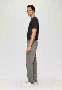 Zwarte t-shirt met korte mouwen, grijze sweatpants met zijzakken en witte sneakers. Model staat in profiel tegen een neutrale achtergrond.