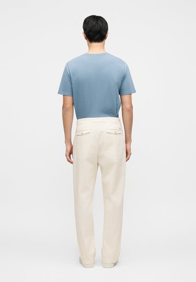 Ανοιχτό μπλε κοντομάνικο μπλουζάκι συνδυασμένο με κρεμ χρώματος χαλαρά παντελόνια. Τα παντελόνια διαθέτουν δύο πίσω τσέπες με κουμπιά.