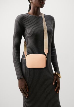 Kobieta w dopasowanej, szarej, prążkowanej sukience, nosząca jasnoróżową torebkę na ramię z szerokim beżowym paskiem oraz złotą bransoletkę na prawej ręce.