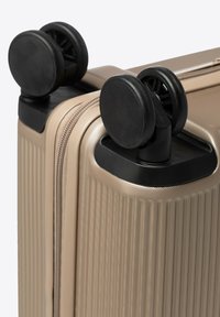 Beige harde kofferhoek met dubbele zwarte spinnerwielen en getextureerde verticale ribbels.