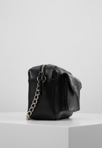 Borsa in pelle nera con chiusura a zip, tracolla a catena e un pannello goffrato testurizzato sul lato. Presenta una forma rettangolare elegante.