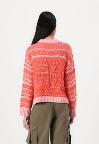 Knit sweater in coral and pink hues, featuring textured patterns, ribbed cuffs, and a relaxed fit. Back view shows intricate designs.