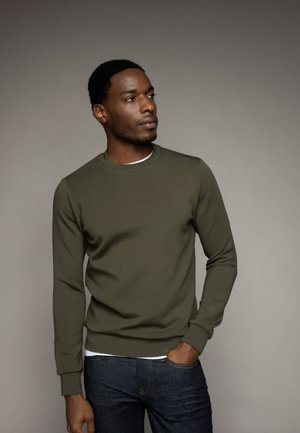Olijfgroen sweatshirt met lange mouwen en een ronde hals, gemaakt van een gladde stof. Combinatie met donkerblauwe jeans.