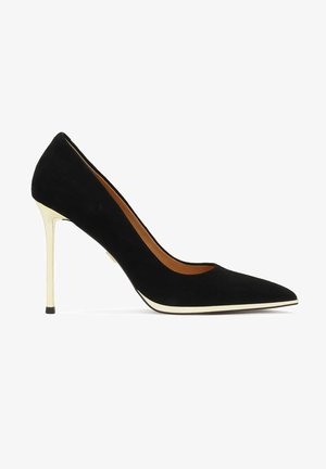 Scarpa nera in suede con tacco alto e punta affusolata, caratterizzata da un tacco dorato a contrasto e una bordatura bianca lungo la suola.