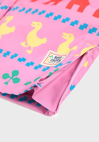 Lys pink stof med gule andemønstre, blå og grønne geometriske former, samt et lille mærke med "BOBO CHOSES" nær en lynlåskant.