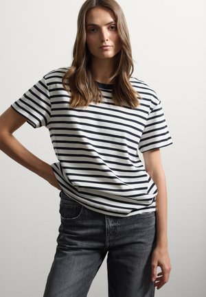 Gestreepte t-shirt met korte mouwen in wit en marineblauw. Katoenen stof, relaxte pasvorm, ronde hals. Gecombineerd met donker gewassen jeans.