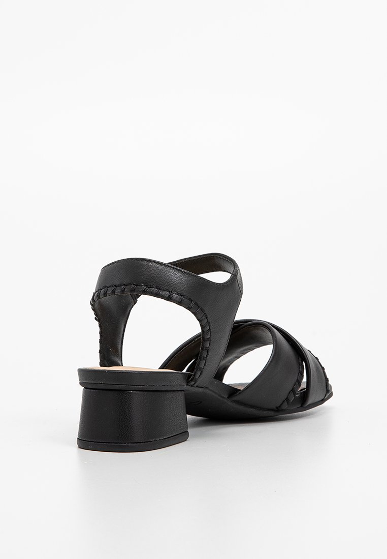 Sandalias de cuero negro con correas entrecruzadas y un bajo tacón cuadrado, con un detalle trenzado a lo largo del borde y una textura suave.