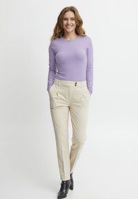 Lichtpaarse lange mouwen top gecombineerd met crèmekleurige op maat gemaakte broek, met twee voortassen en twee knoopaccenten. Zwarte enkellaarsjes.