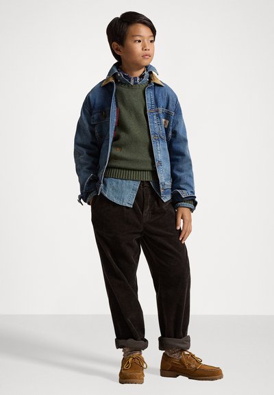 Denim jacket with beige collar, green sweater layered over a light blue shirt, brown corduroy pants, and tan shoes with laces.