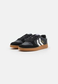 Black sneakers with suede and leather materials, featuring white chevron stripes, rubber gum sole, round toe, and traditional lace-up design.