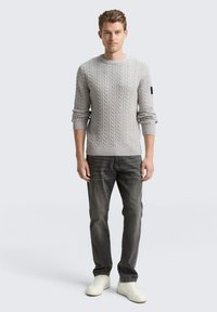 Grijze kabelgebreide trui met een ronde hals, lange mouwen en een slanke pasvorm, gecombineerd met donkergrijze jeans en witte sneakers.