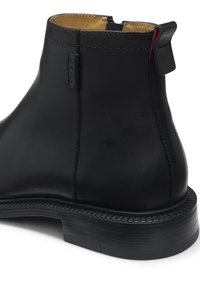 Bottine en cuir noir à bout arrondi, avec une languette à l'arrière et un petit talon empilé, présentant des coutures détaillées et une finition lisse.