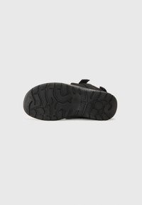 Black sandal sole with a textured rubber surface, featuring a tread pattern for grip, and adjustable straps for fit.