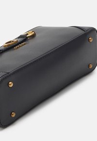 Černá kožená kabelka se zlatými kovovými doplňky, viditelným šitím a ochrannými kovovými nožkami na dně. Na boku je detail s logem.