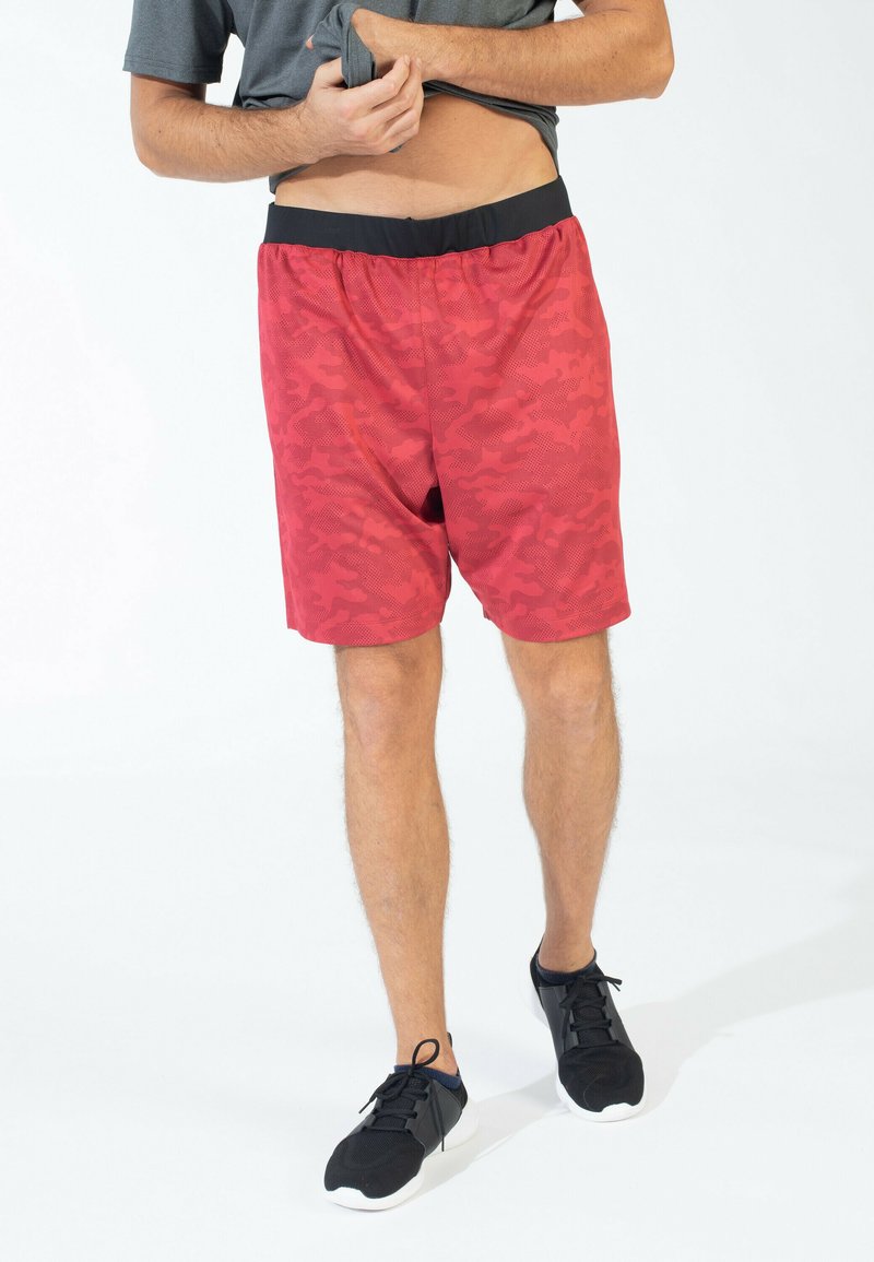 Shorts deportivos de camuflaje rojo con una cintura elástica negra, hechos de una tela ligera, combinados con zapatillas deportivas negras.
