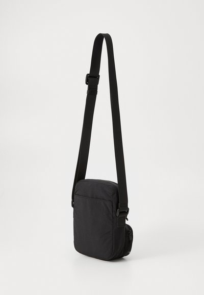 Sac bandoulière noir en tissu durable. Présente une forme rectangulaire plate, une bandoulière réglable et une poche latérale zippée.