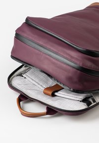 Borsa per laptop color bordeaux con esterno liscio, zip nera e manico in pelle beige. Contiene un interno foderato con un motivo a scacchi.