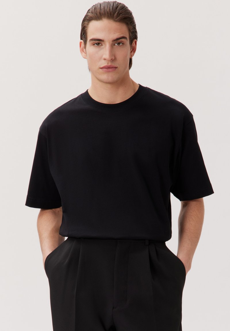 T-shirt noir à manches courtes en coton doux, avec un col rond et une coupe décontractée. Pas de motifs ni de embellissements visibles.