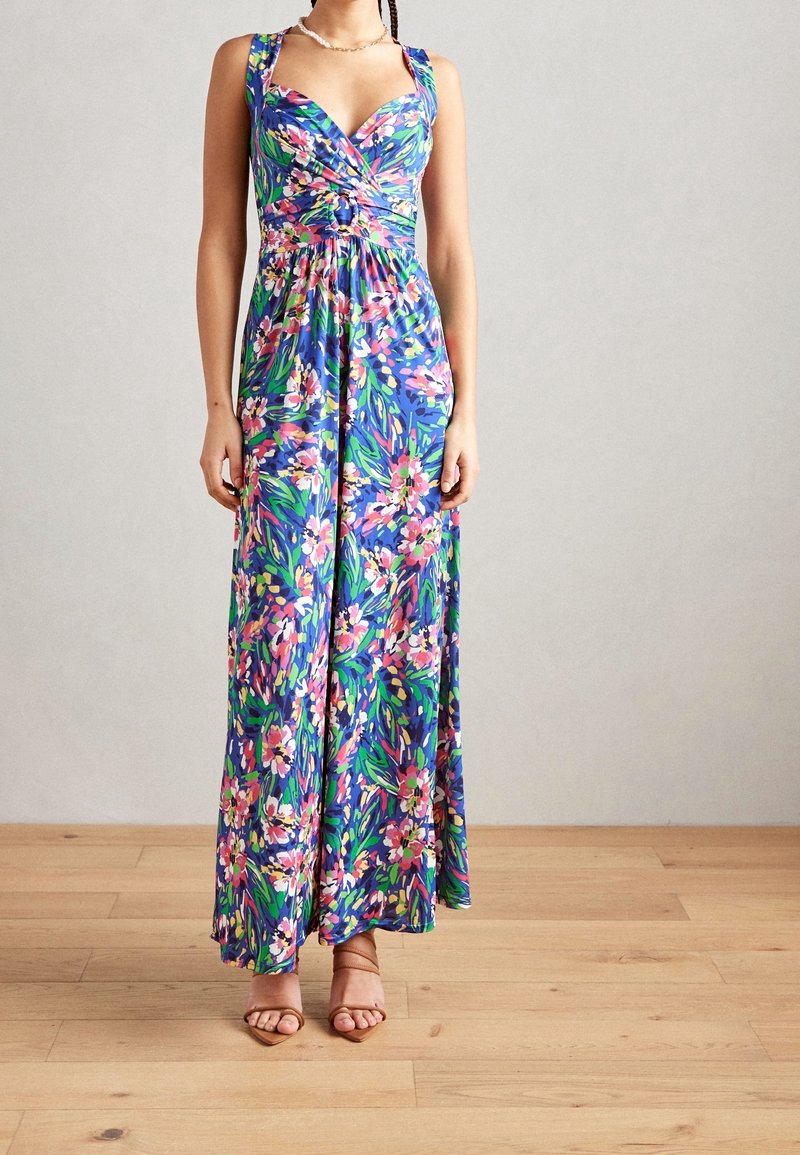 Maximekkossa sinisestä kankaasta, jossa on pinkkejä ja vihreitä kukkakuoseja. Säädettävät olkaimet ja mukautuva yläosa yhdistyvät kauniiseen, alas virtaavaan helmaan.