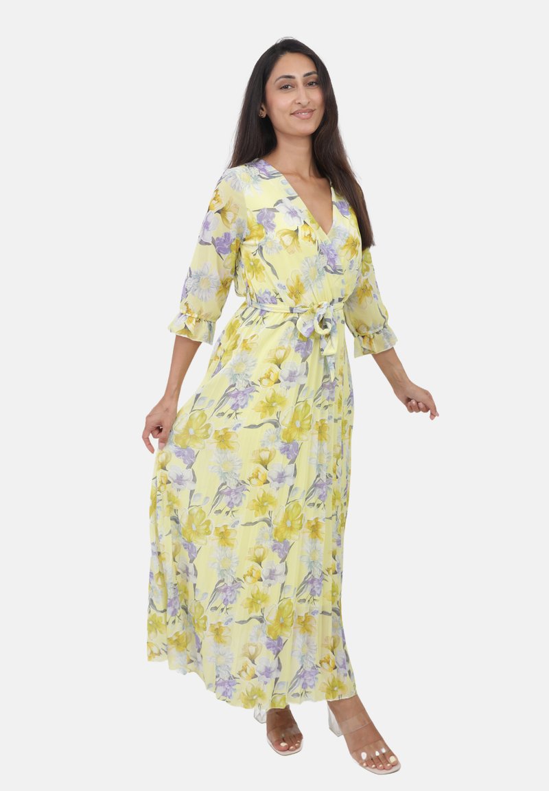 Maxi kjole i lys gul med blomsterprint i lilla og gul. Har V-hals, trekvartlange ærmer og en bundet talje. Glat stof.