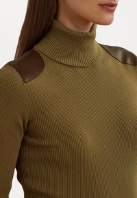 Col roulé côtelé vert olive avec des accents en cuir marron sur les épaules, présentant un design ajusté et une texture douce.