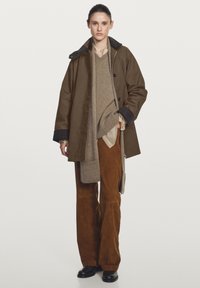 Brown outer jacket with a dark collar, beige sweater, and brown suede pants. Features a relaxed fit, large buttons, and layered textures.