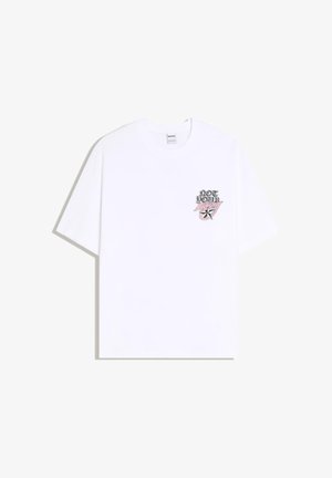 Bílé tričko s krátkým rukávem s malou grafikou na hrudi, která obsahuje text „NOT YOUR“, růžové stylizované slovo a černo-růžový motiv hvězdy na levé straně.