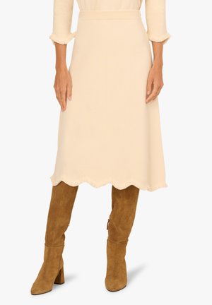 Beige, Midikleid aus weichem Stoff mit einer gezackten Saumkante und fransigen Rändern, kombiniert mit taupefarbenen Wildleder-Stiefeln bis zum Knie.