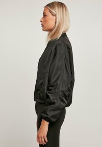 Black bomber jacket made from smooth fabric with elastic cuffs and a gathered hem, featuring a zip closure and a relaxed, cropped design.