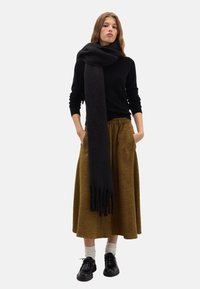 Schwarzer Wollschal um den Hals drapiert, kombiniert mit einem schwarzen Pullover und einem braunen knielangen Rock, abgerundet mit schwarzen Schuhen und weißen Socken.