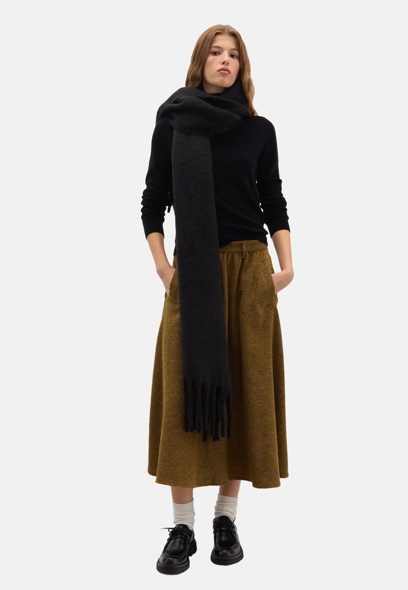 Sciarpa di lana nera appoggiata attorno al collo, abbinata a un maglione nero e a una gonna marrone fino al ginocchio, completata con scarpe nere e calzini bianchi.