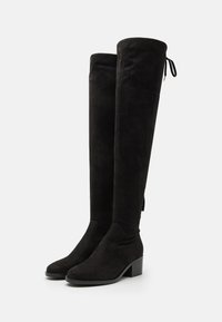 Botas negras por encima de la rodilla hechas de suave ante. Tacón grueso, punta afilada y detalle de lazo ajustable en la parte trasera. Textura suave sin patrones visibles.