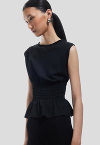 Top peplum negro con un acabado texturizado, que presenta mangas cortas y detalles fruncidos en la cintura. Tela suave con una silueta ajustada.