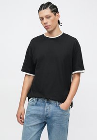 Zwart katoenen T-shirt met korte, opgerolde witte manchetten en een ronde halslijn, gecombineerd met lichtblauwe denim jeans met een milde wassing en voorzakdetail.