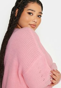 Ljust rosa oversize stickad tröja med en mjuk textur, med en lös passform och subtilt stickat mönster. Accentuerad med ribbade ärmslut.