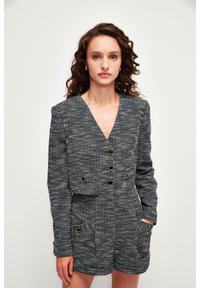 Vestido blazer texturizado en blanco y negro con escote en V, diseño corto, detalles de botones dorados y bolsillos laterales.