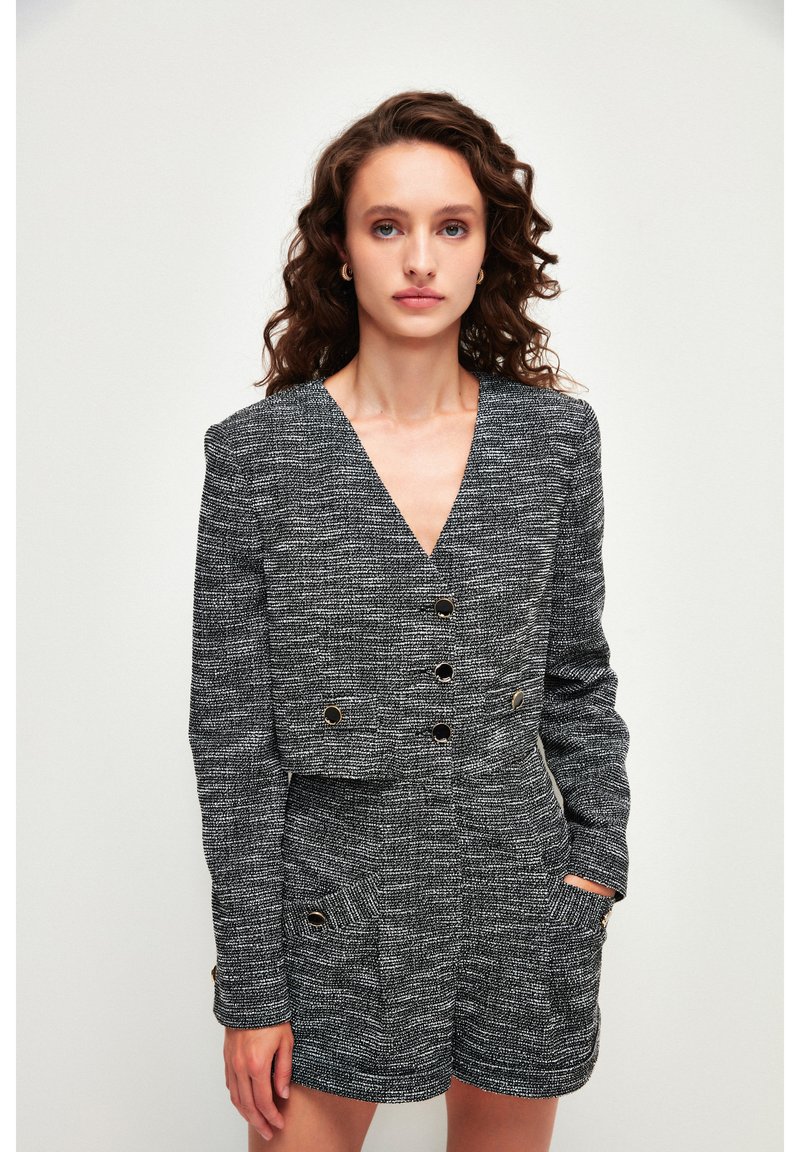 Vestido blazer texturizado en blanco y negro con escote en V, diseño corto, detalles de botones dorados y bolsillos laterales.