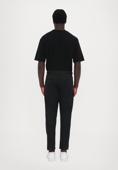 Black cotton t-shirt with short sleeves, paired with black pants featuring side pockets and a slim fit, complemented by white sneakers.