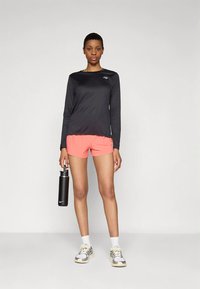 Melna sporta krekls ar garām piedurknēm, spilgti rozā šorti, balti zeķes un sporta apavi. Tur melnu ūdens pudeli. Tīrs dizains, moderns piegriezums.