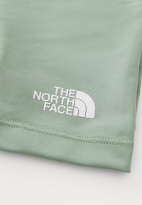 Svijetlozelena tkanina s glatkom teksturom, s istaknutim bijelim logotipom "THE NORTH FACE" i polukružnim dizajnom.