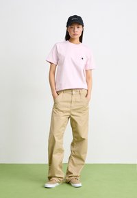 Rosa kortärmad t-shirt med ficka och logotyp, beige vida byxor och bruna skor, kompletterat med en svart keps med vit text.