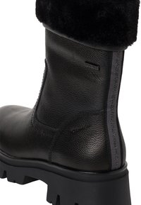 Bottine en cuir noir avec une finition texturée, panneau latéral élastique gris et revers en fausse fourrure noire. Semelle en caoutchouc noir épaisse avec un détail antidérapant.