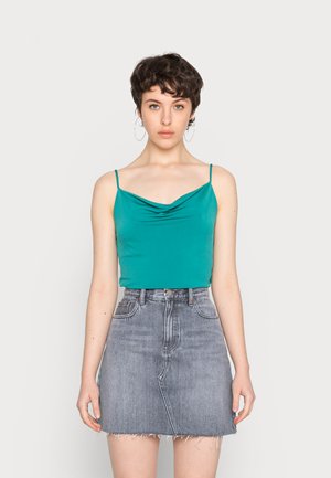 Top sem mangas em verde-água com decote drapeado, combinado com uma saia mini em denim cinza com bainha desfiada e bolsos frontais.