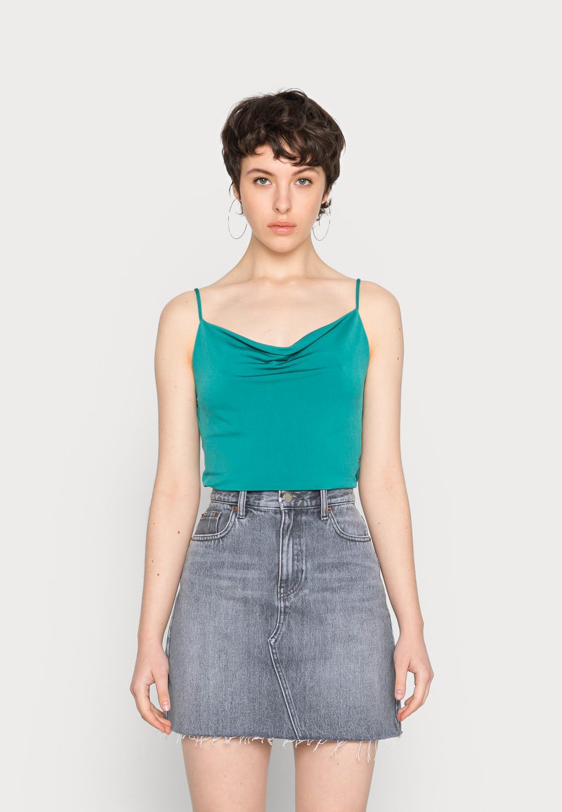 Top sem mangas em verde-água com decote drapeado, combinado com uma saia mini em denim cinza com bainha desfiada e bolsos frontais.